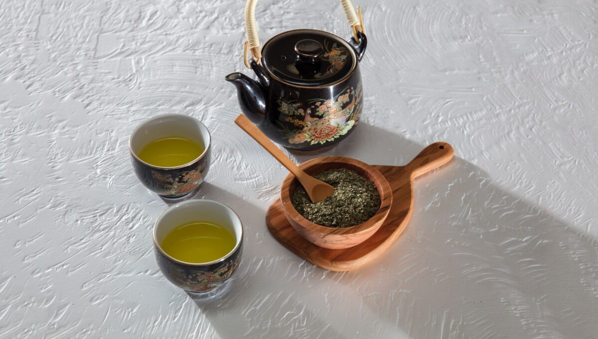 A tea pot and 2 cups with some green tea herbs on a white background