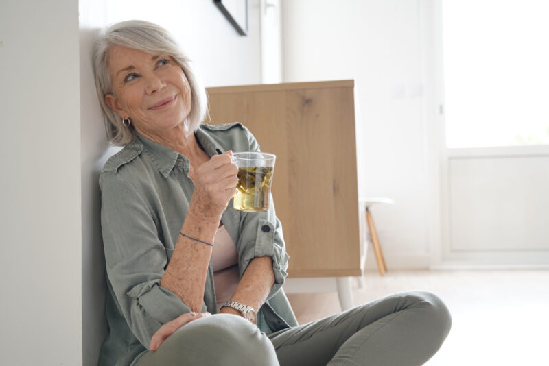 A happy, healthy mature lady sits looking happy and rested with a cup of herbal tea.