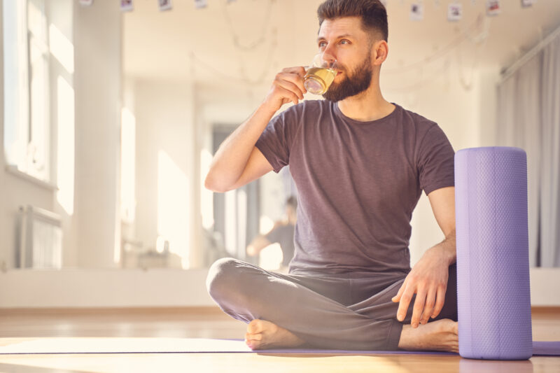 A man sits on yoga mat sipping a herbal tea blend to support his health and fitness regime.