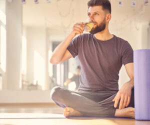 A man sits on yoga mat sipping a herbal tea blend to support his health and fitness regime.