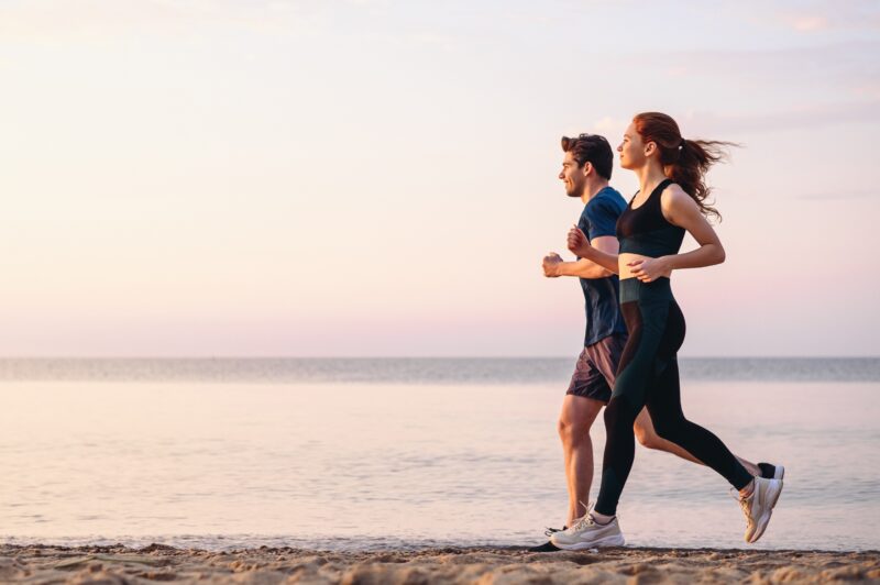 A man and woman running along the beach at sunset in the summer.