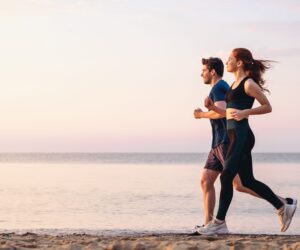 A man and woman running along the beach at sunset in the summer.