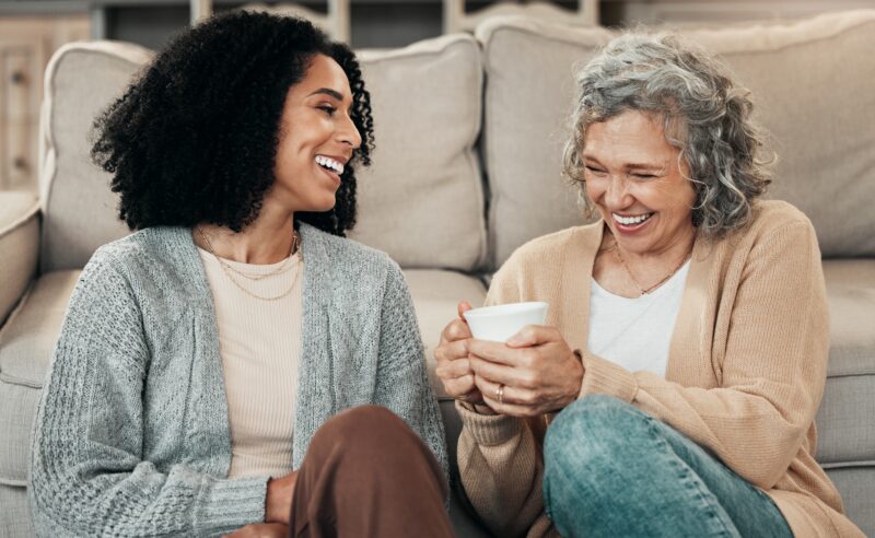 A young woman and a mature woman sit enjoying a cup of tea together