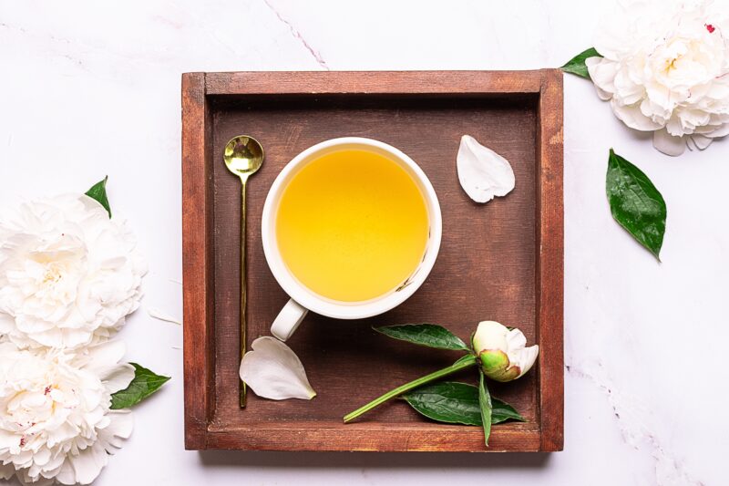 A cup of white peony tea presented on a tray with white peony flowers