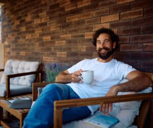 A man sits drinking a cup of herbal tea, looking healthy, happy, and relaxed.