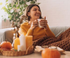 A lady sits drinking a cup of herbal tea surrounding by autumnal decor.