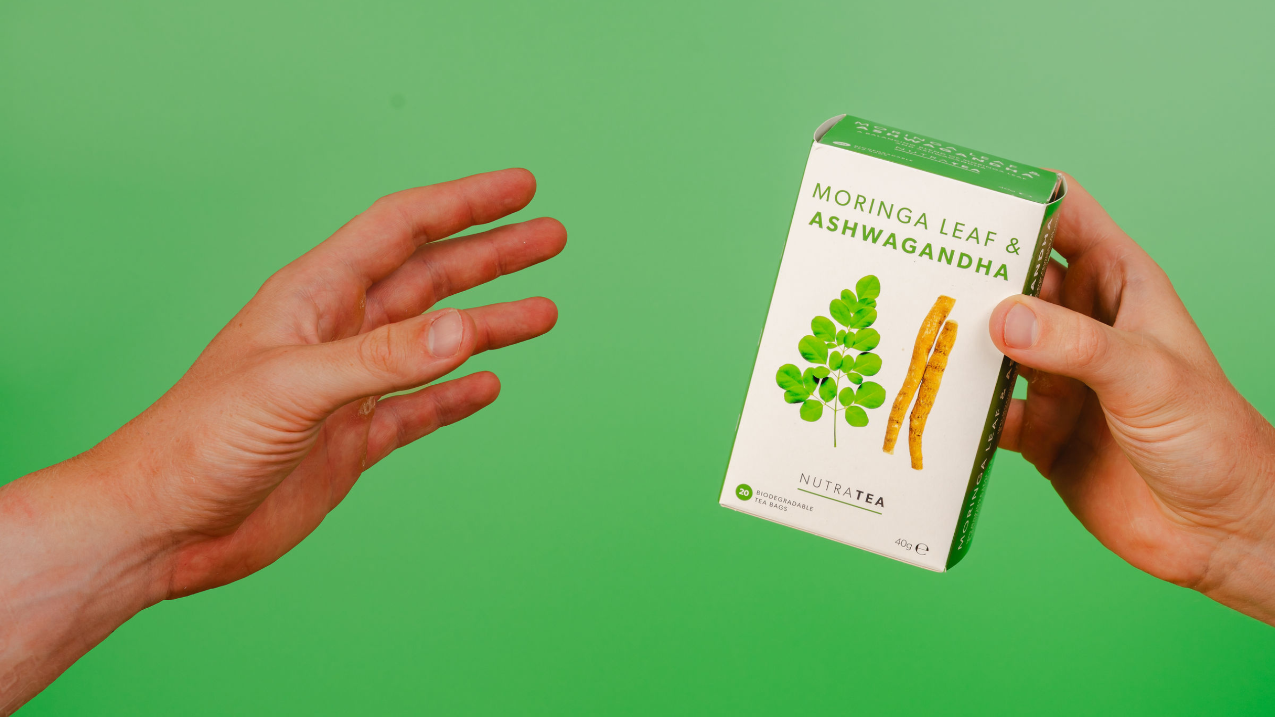 Two hands holding a box of NutraTea Moringa Leaf and Ashwagandha herbal blend tea bags