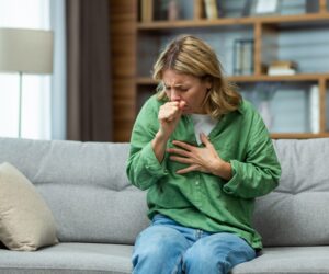 a woman sits coughing on the sofa