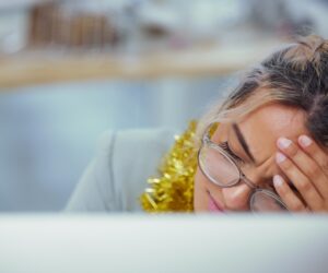 A woman holds her head in her hands suffering from holiday burnout