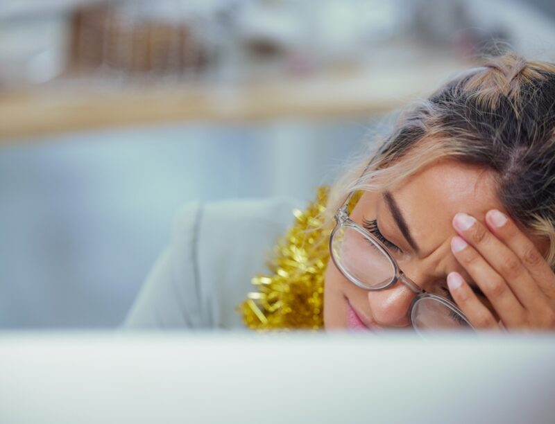A woman holds her head in her hands suffering from holiday burnout