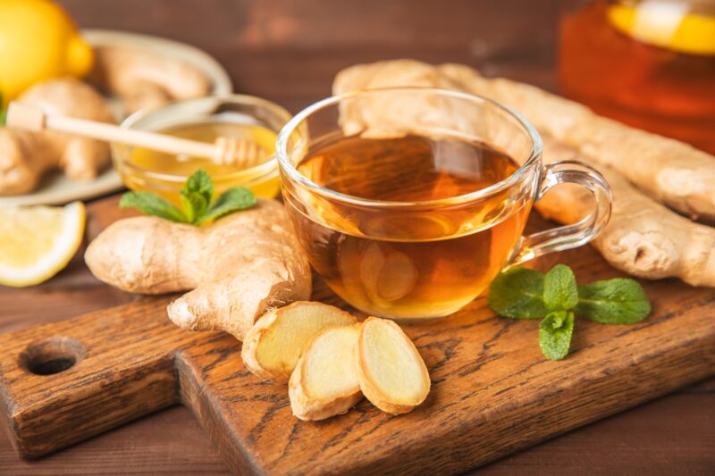 A cup of ginger herbal tea surrounded by fresh ginger